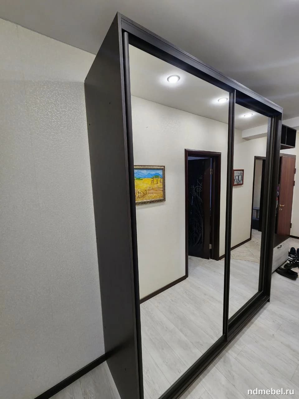 Это современный шкаф-купе с тремя большими зеркальными дверцами в темном (вероятно, венге или черном) корпусе. Мебель выполнена в минималистичном стиле и предназначена для хранения одежды.