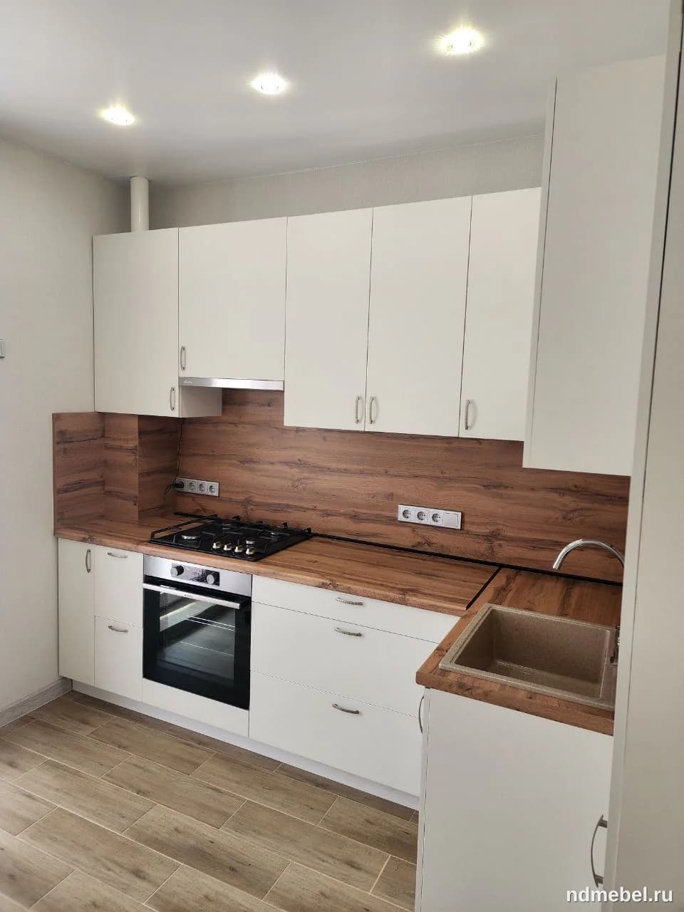 Современная прямая кухонная мебель выполнена в минималистичном стиле с гладкими белыми фасадами и контрастной столешницей, имитирующей текстуру натурального дерева. Гарнитур включает встроенную бытовую технику и сочетает функциональность с чистым, светлым дизайном.
