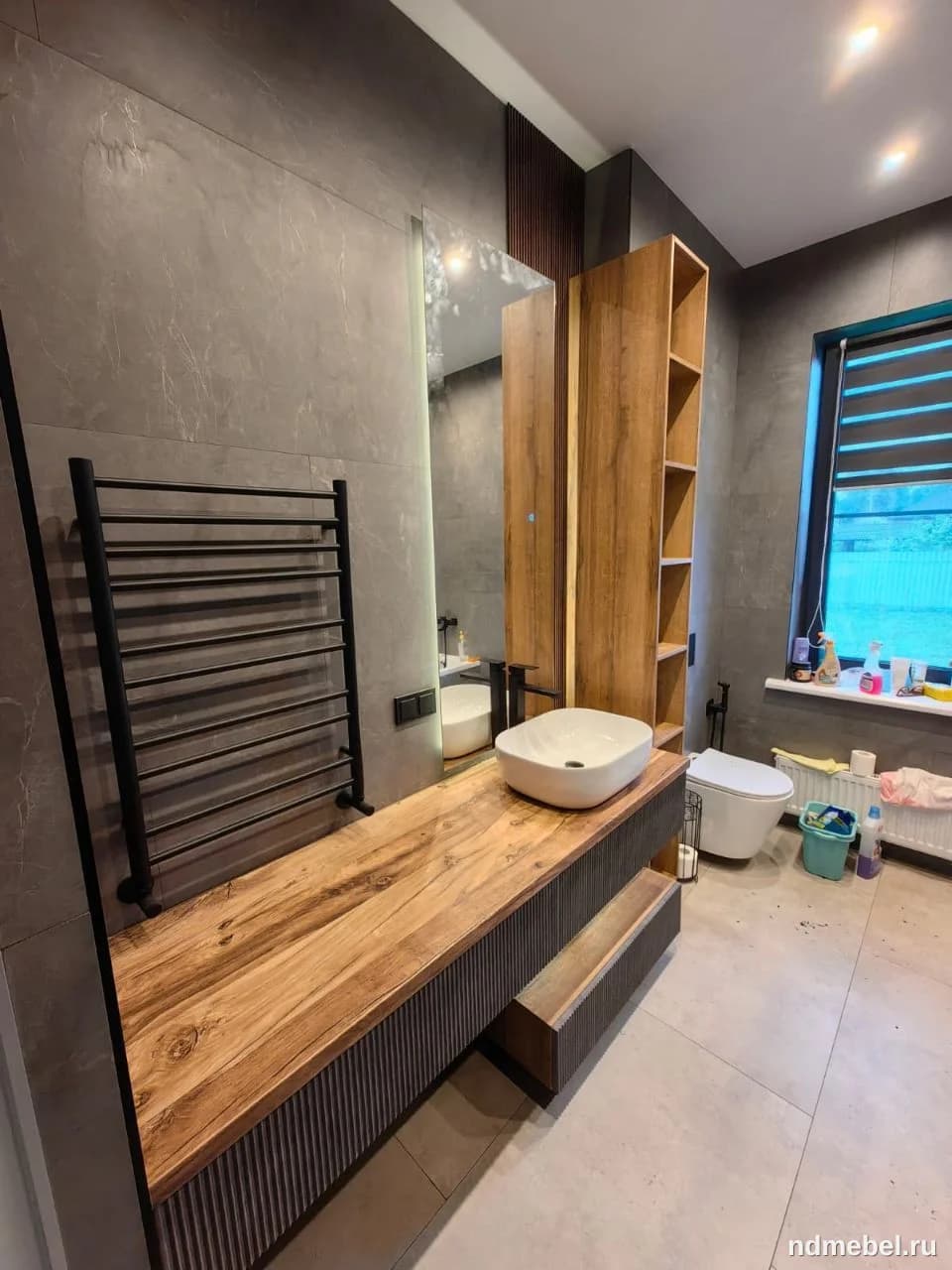 Современная и стильная мебель для ванной комнаты, включающая широкую столешницу из натурального дерева с выраженной текстурой и темный рельефный фасад. Ансамбль дополнен высоким открытым стеллажом из МДФ под дерево и белой накладной раковиной, подчеркивая индустриально-эко стиль интерьера.