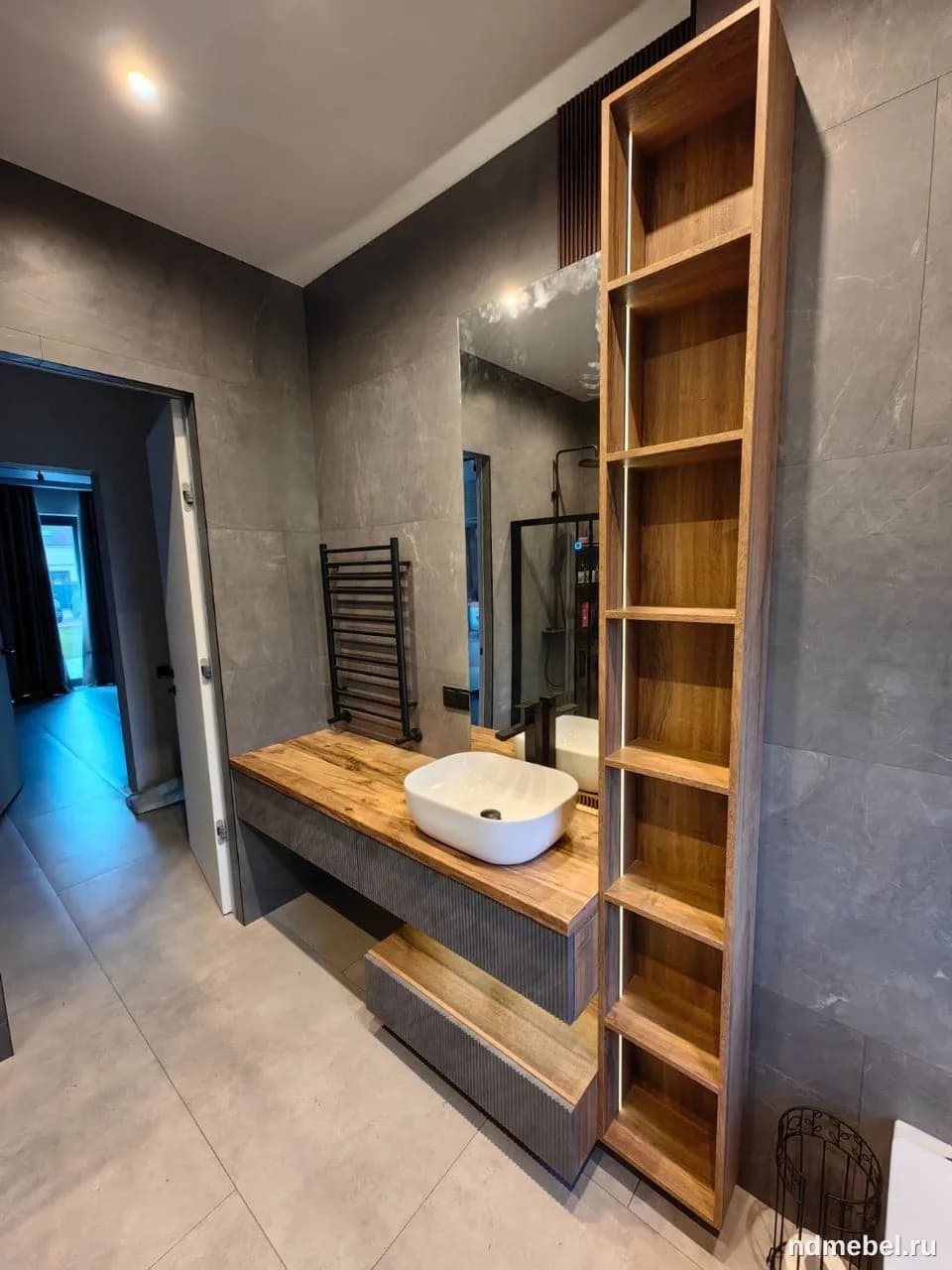 Современная дизайнерская тумба под раковину с деревянной столешницей и открытым высоким стеллажом, выполненная в стиле лофт или минимализм, с контрастом натурального дерева и темных текстурированных фасадов.
