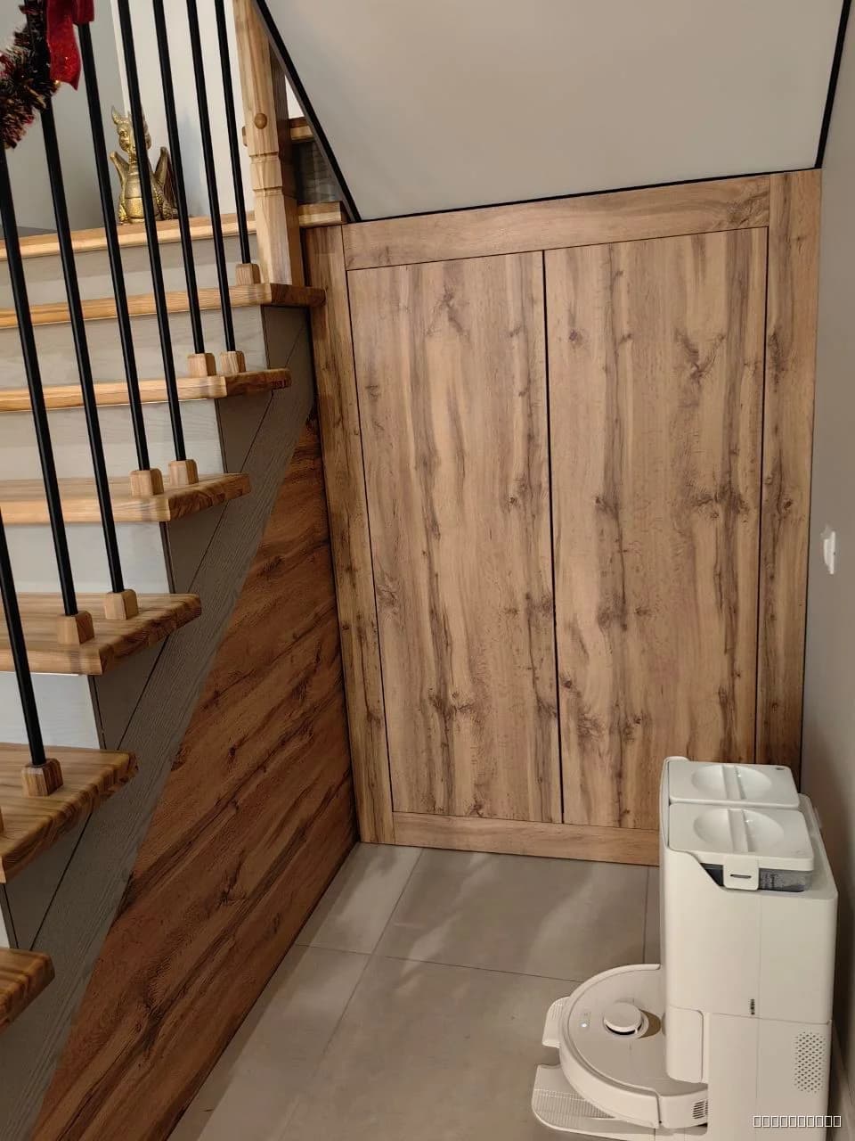 Деревянный шкаф с двумя дверями, выполненный из светлого дерева, в современном стиле, установленный рядом с лестницей.